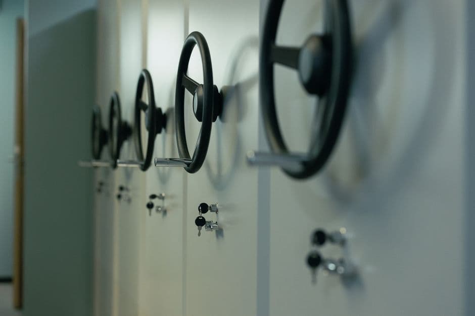 A row of mobile storage cabinets seen at an angle, each with a large black rotating handwheel and a small keyed lock, receding into a blurred office corridor.
