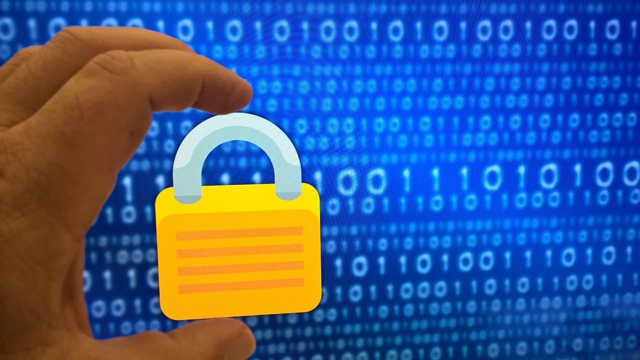 A hand holding a padlock icon in front of a screen of blue binary code