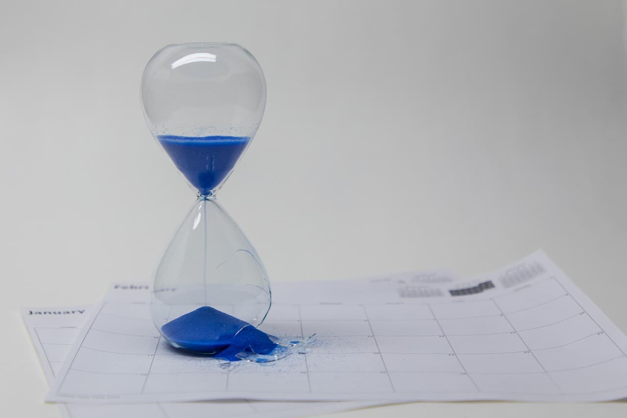 An hourglass with sand running through it, against a blue background