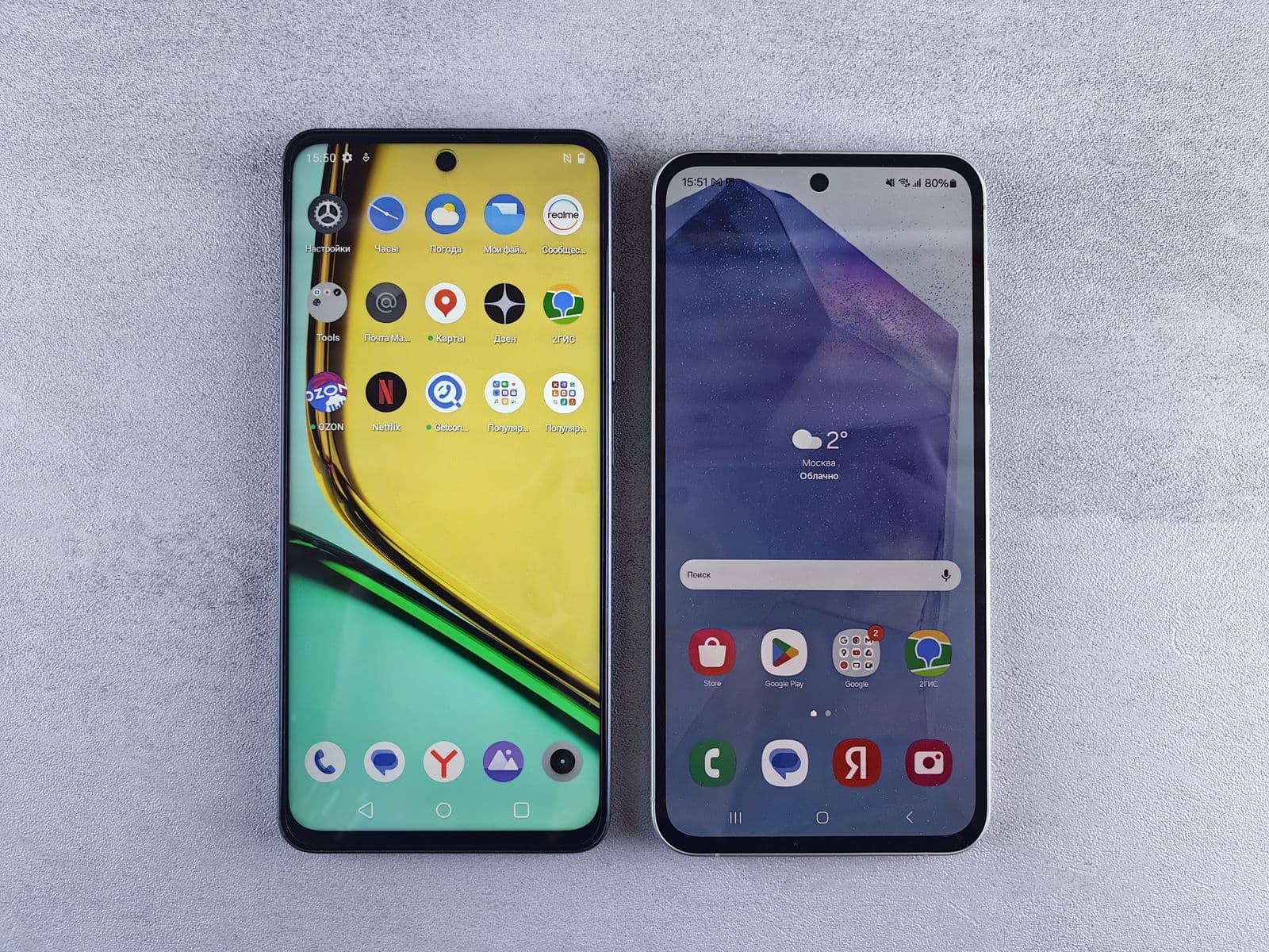 Two modern smartphones photographed from above, side by side on a textured grey surface. The left screen shows a yellow and green wallpaper behind a grid of colourful icons, the right shows a purple and blue wallpaper with a weather widget reading 2 degrees, a search bar and a dock of icons. Both screens are on and unlocked, which is the situation this whole article depends on.