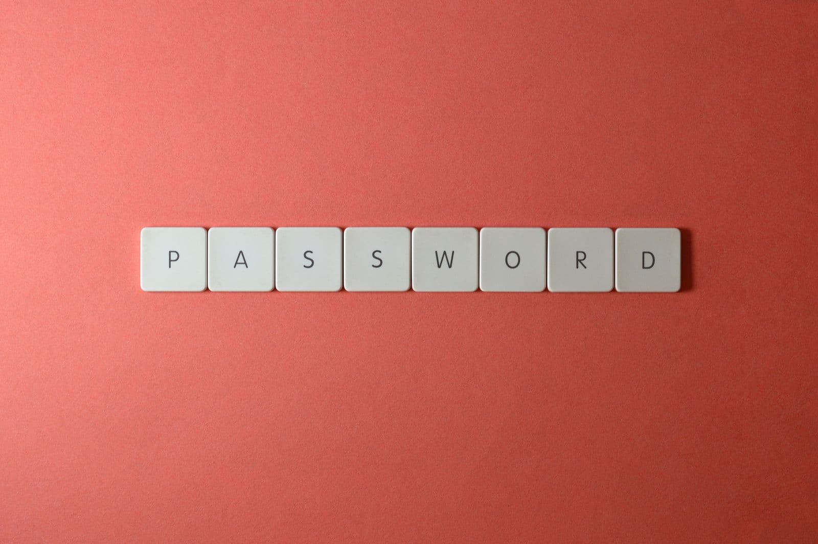 Peças de teclado brancas dispostas para soletrar uma palavra-passe. O password spraying aproveita-se de palavras-passe comuns e previsiveis - o oposto das longas sequencias aleatorias que um gestor de palavras-passe cria.