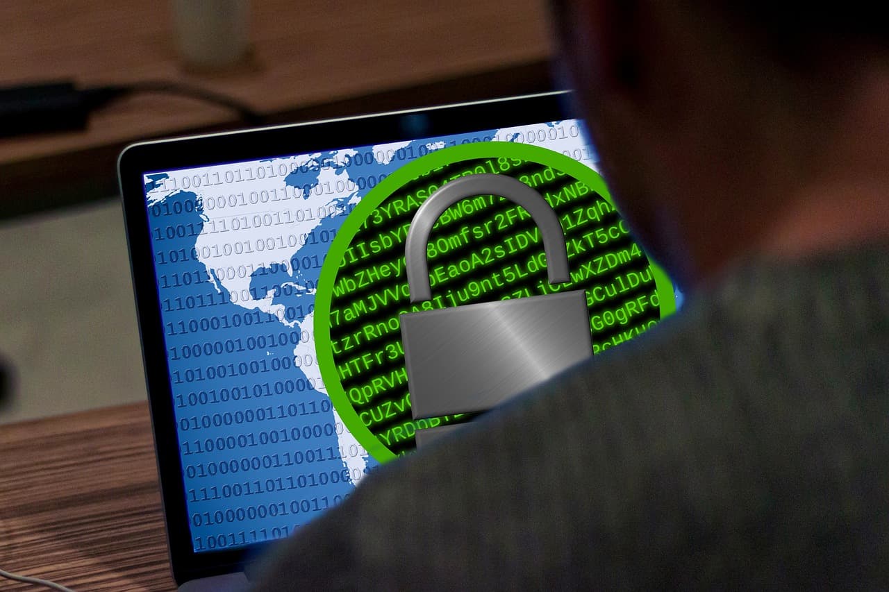 Eine Person vor einem Laptop, dessen Bildschirm ein Vorhängeschloss über einer aus Binärziffern gezeichneten Weltkarte zeigt