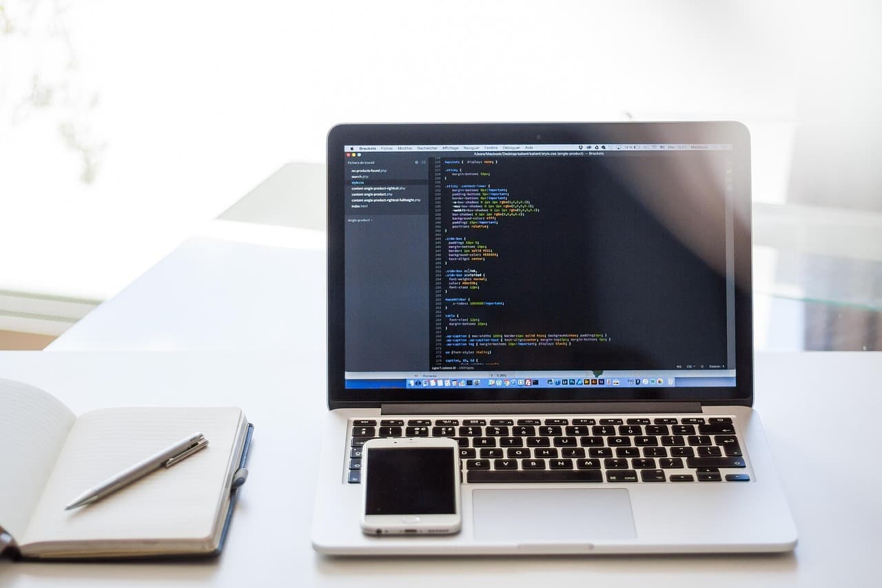 Un portatile aperto su un editor di codice con uno smartphone appoggiato sulla tastiera. Una chiave di sicurezza va registrata su ogni dispositivo da cui accedi.